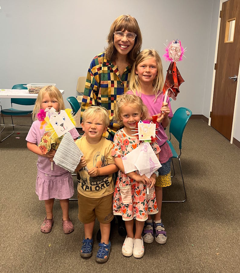 A woman and a group of children smiling and holding puppets